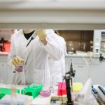 Cientista de jaleco e luvas manuseia amostras em um laboratório moderno.