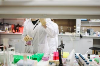 Cientista de jaleco e luvas manuseia amostras em um laboratório moderno.
