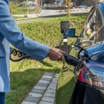 Pessoa conecta um carro elétrico a uma estação de recarga ao ar livre.