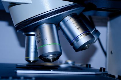 Close de um microscópio examinando uma lâmina com amostra em ambiente de laboratório.